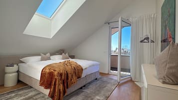 A bedroom with a skylight, a bed with a brown blanket, a bedside table, and a view through a sliding glass door.