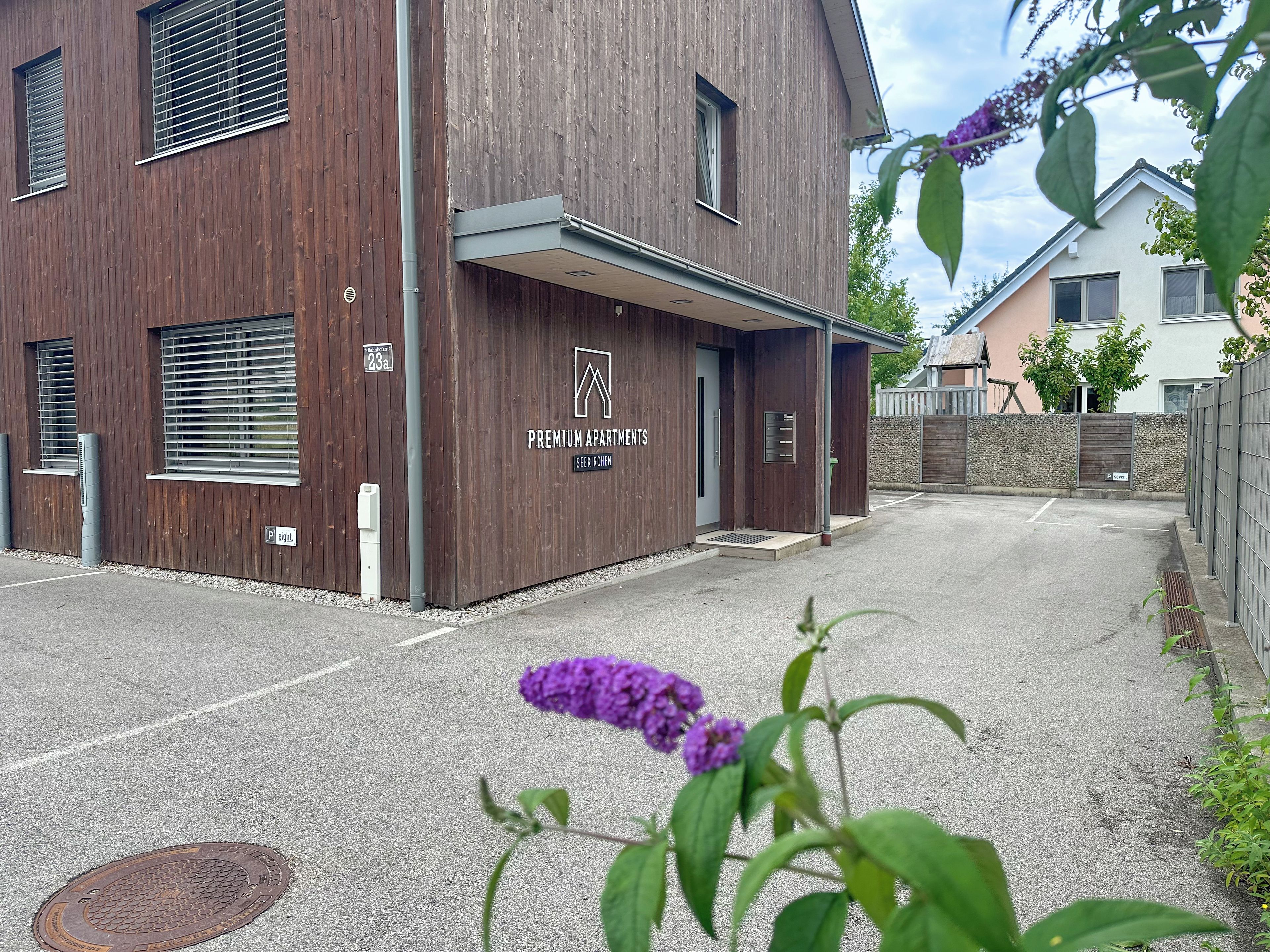 A modern building with a wooden facade, a sign indicating 'Premium Apartments,' and a gated parking area.