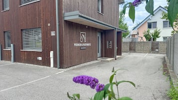 A modern building with a wooden facade, a sign indicating 'Premium Apartments,' and a gated parking area.