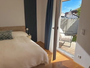 A bedroom with a bed, a nightstand, a lamp, and a view of the outside.