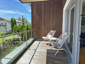 A balcony with two white lounge chairs, a glass balustrade, and a wooden deck.