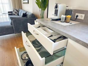 A modern kitchen with white cabinetry, a coffee machine, and a dining area with a grey sofa.