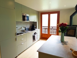 Een keuken met een magnetron, oven en gootsteen. Een houten deur leidt naar een balkon met uitzicht.