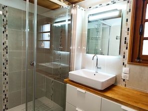 Ein modernes Badezimmer mit einer gläsernen Dusche, einem weißen Waschbecken mit Holzablage und einem Spiegel darüber.