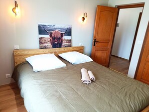 Een bed met een houten hoofdbord, twee witte kussens en een opgerolde handdoek.