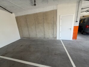 An empty parking garage with concrete walls and a white door. - New, cosy and adult only app in a beautiful village with a lake view (Béznar)