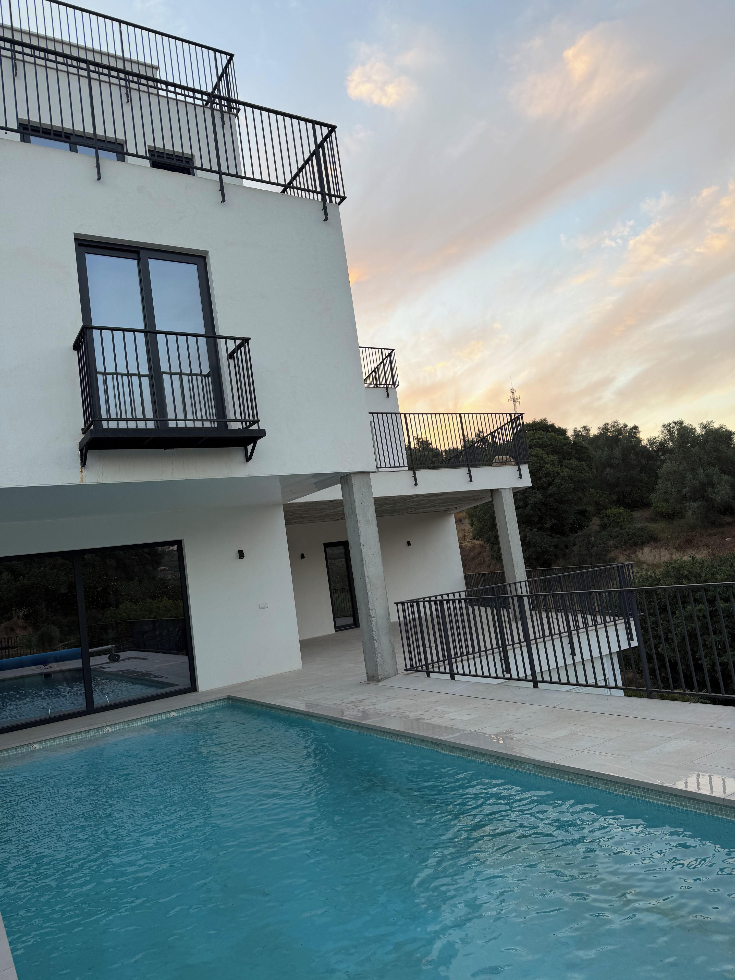 A modern two-story building with a swimming pool, balconies, and a clear sky.
