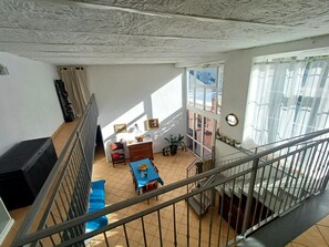 Um quarto com pé direito alto, escada, sala de jantar com mesa e cadeiras, e janela com cortinas.
