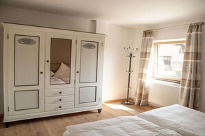 A bedroom with a large wardrobe, a bed, and a window with curtains. - Holiday apartment with 1 bedroom (Hopfen am See)