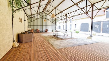 Ein überdachter Außenbereich mit Holzterrasse, Sitzgelegenheiten und einem Tisch auf Rollen.