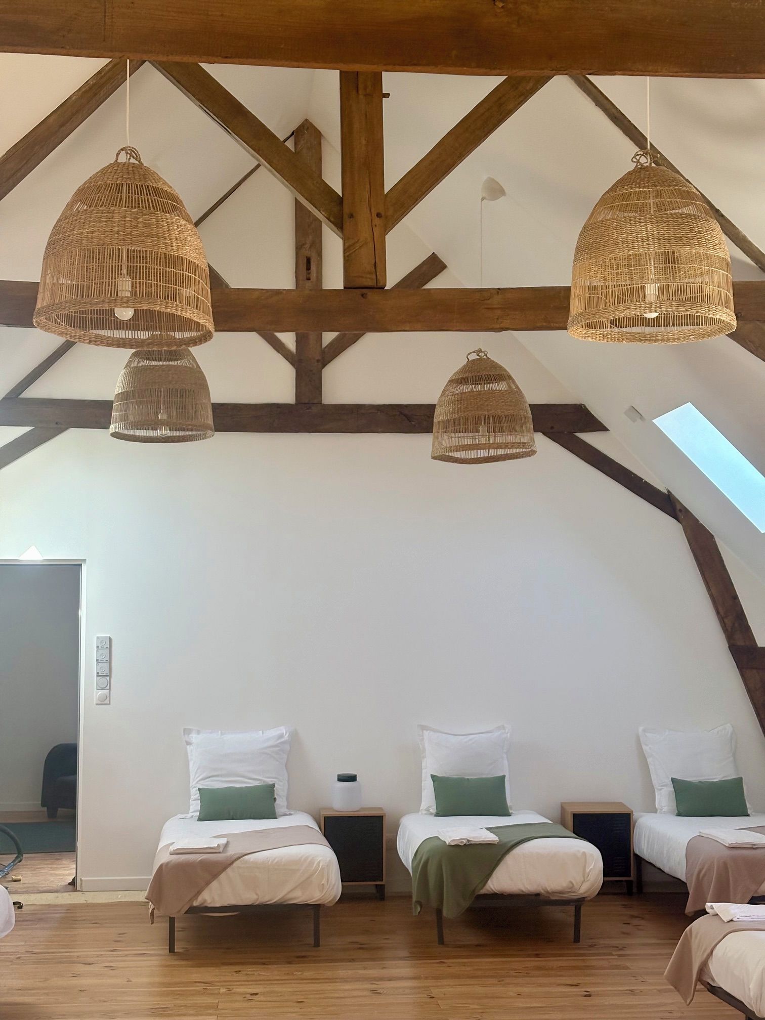 Una habitación con tres camas, vigas de madera y lámparas de techo tejidas.