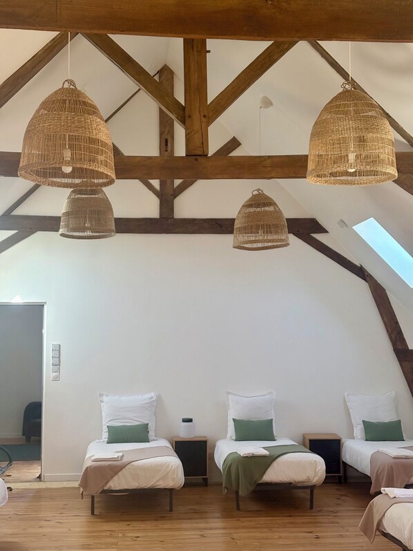 A room with three beds, wooden beams, and woven ceiling lamps.