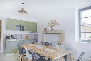A modern kitchen with green cabinets, a dining table with chairs, and a fireplace.