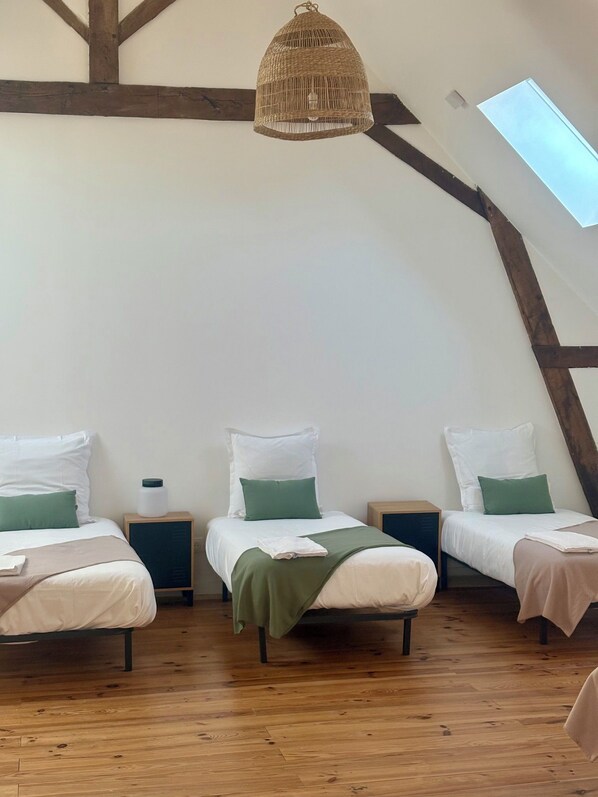 Une pièce chaleureuse et bien éclairée, avec trois lits, un plancher en bois et un plafond en pente doté d’un puits de lumière.