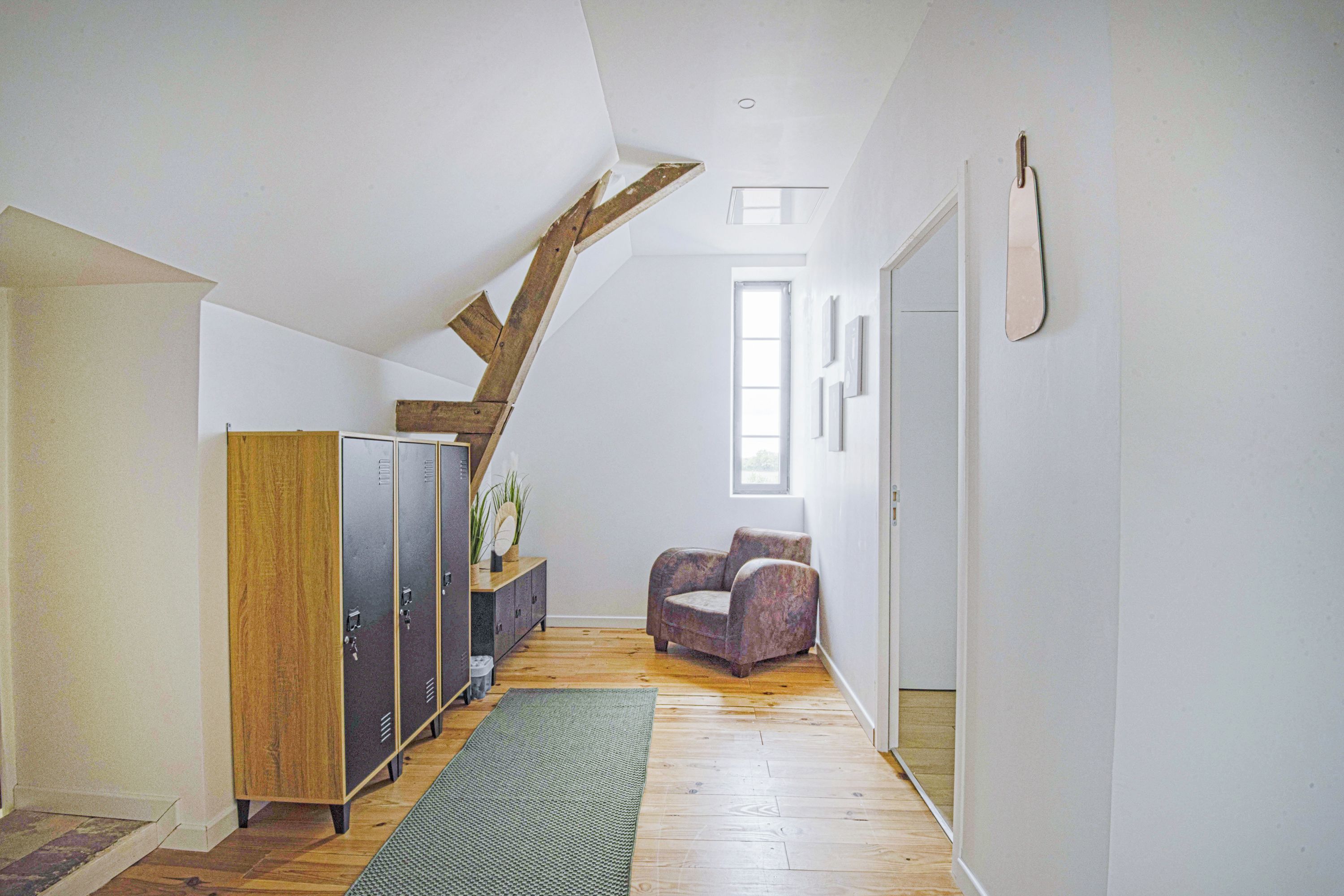 Een hal met een houten trap, een grijze kast, een kamerkleed met patroon en een stoel.