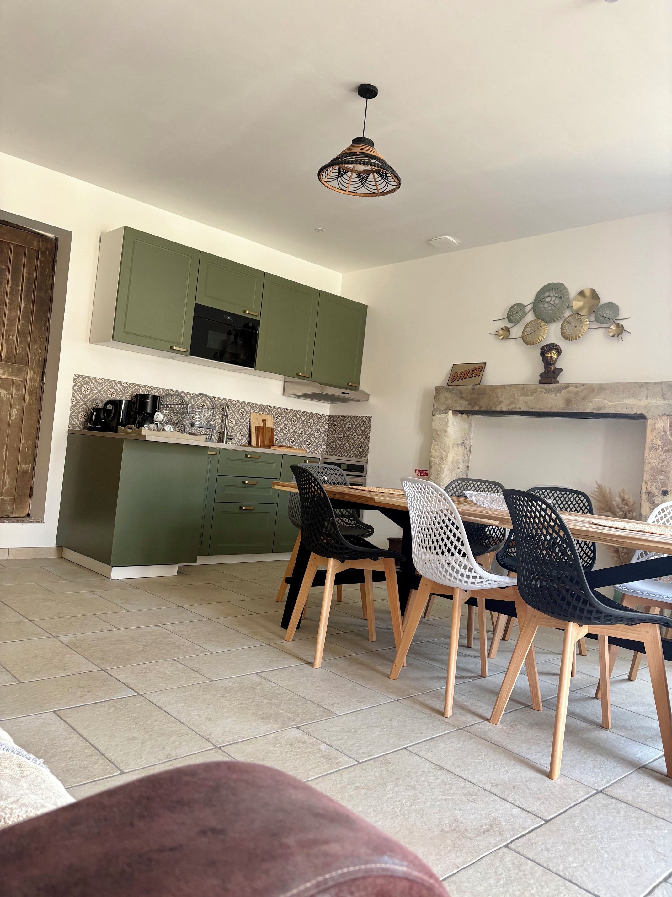 Una cocina moderna con armarios verdes, un comedor con mesa y sillas de madera, y un elemento decorativo sobre la chimenea.