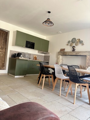 Une cuisine moderne avec des meubles de couleur verte, un coin repas avec une table et des chaises en bois, et un élément décoratif mural au-dessus de la cheminée.