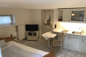 Ein kleines, ordentliches Zimmer mit einem Bett, einem Fernseher, einem Tisch und einem Stuhl.
