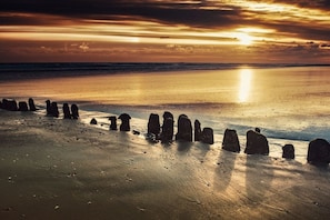 Ein Strand mit Steinkreis im Vordergrund und Sonnenuntergang im Hintergrund.