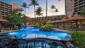 En hotellpool med ett vattenfall, omgiven av palmer och solstolar.