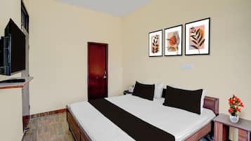 Quarto de hotel com cama, televisão, porta e três quadros na parede.