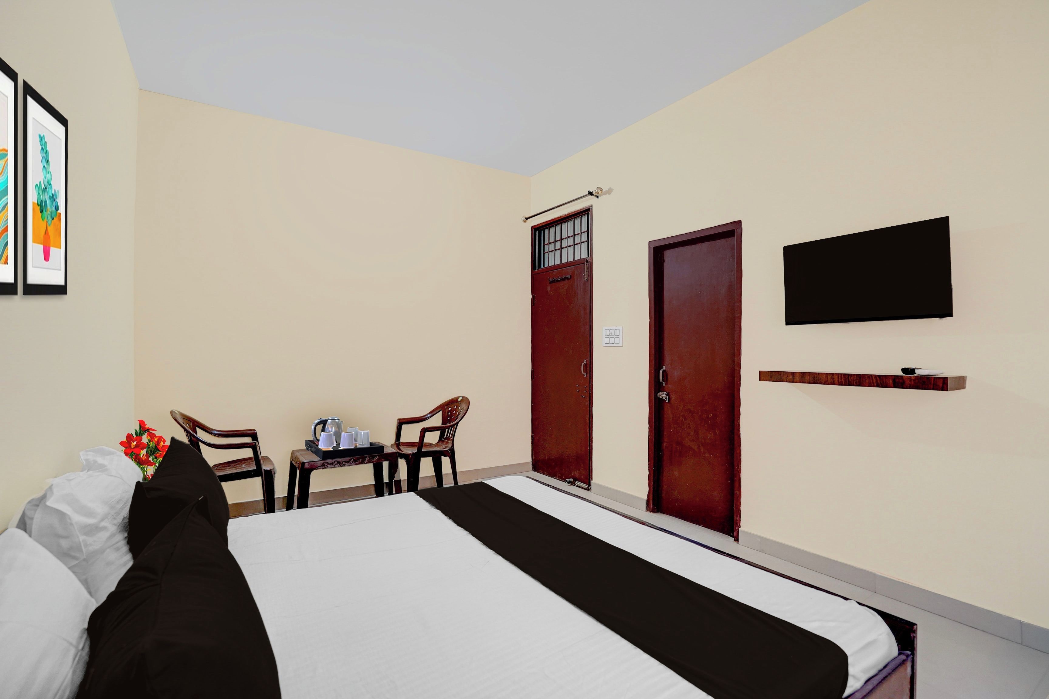 A hotel room with a bed, two chairs, a small table with a kettle, and a TV mounted on the wall.