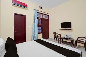 A hotel room with a bed, a TV, a desk with a chair, and a window with curtains.