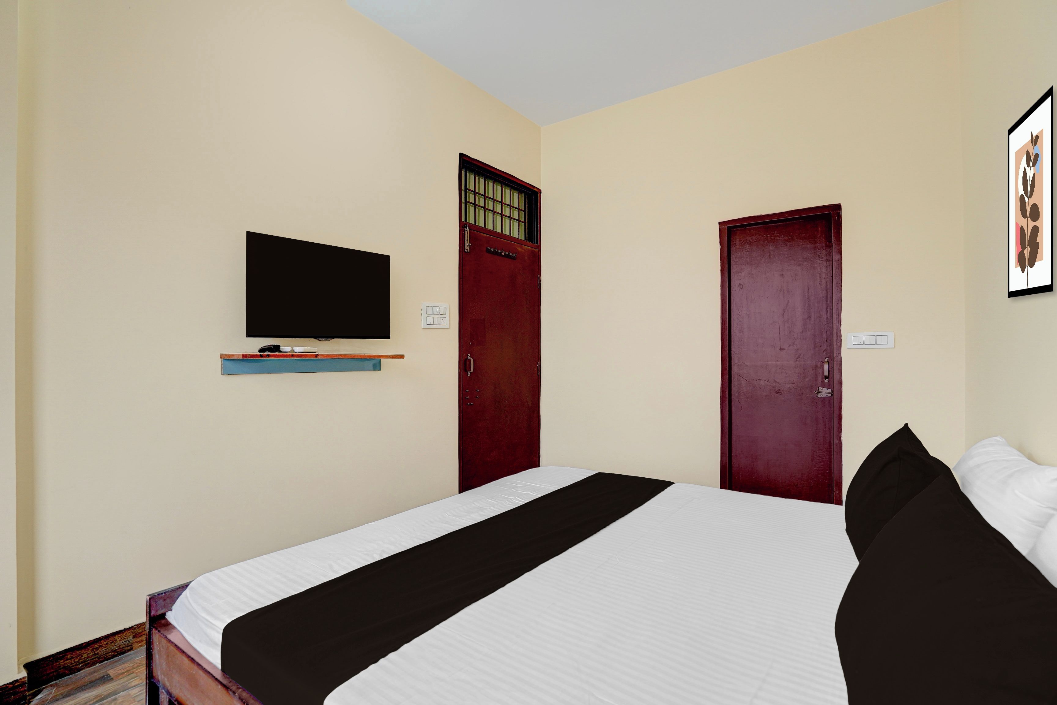 Una habitación con una cama, un televisor montado en la pared y dos puertas.