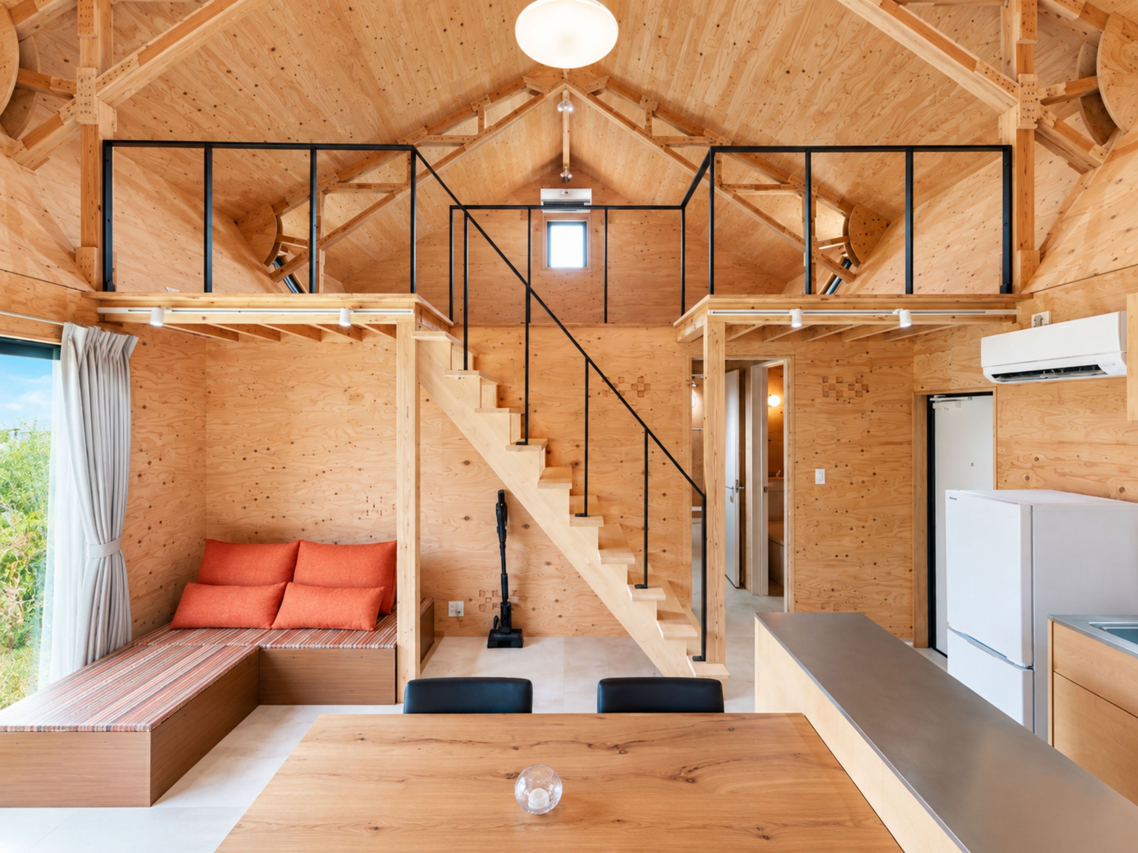 A wooden interior with a staircase, a sofa with cushions, a dining table, and a kitchen area.