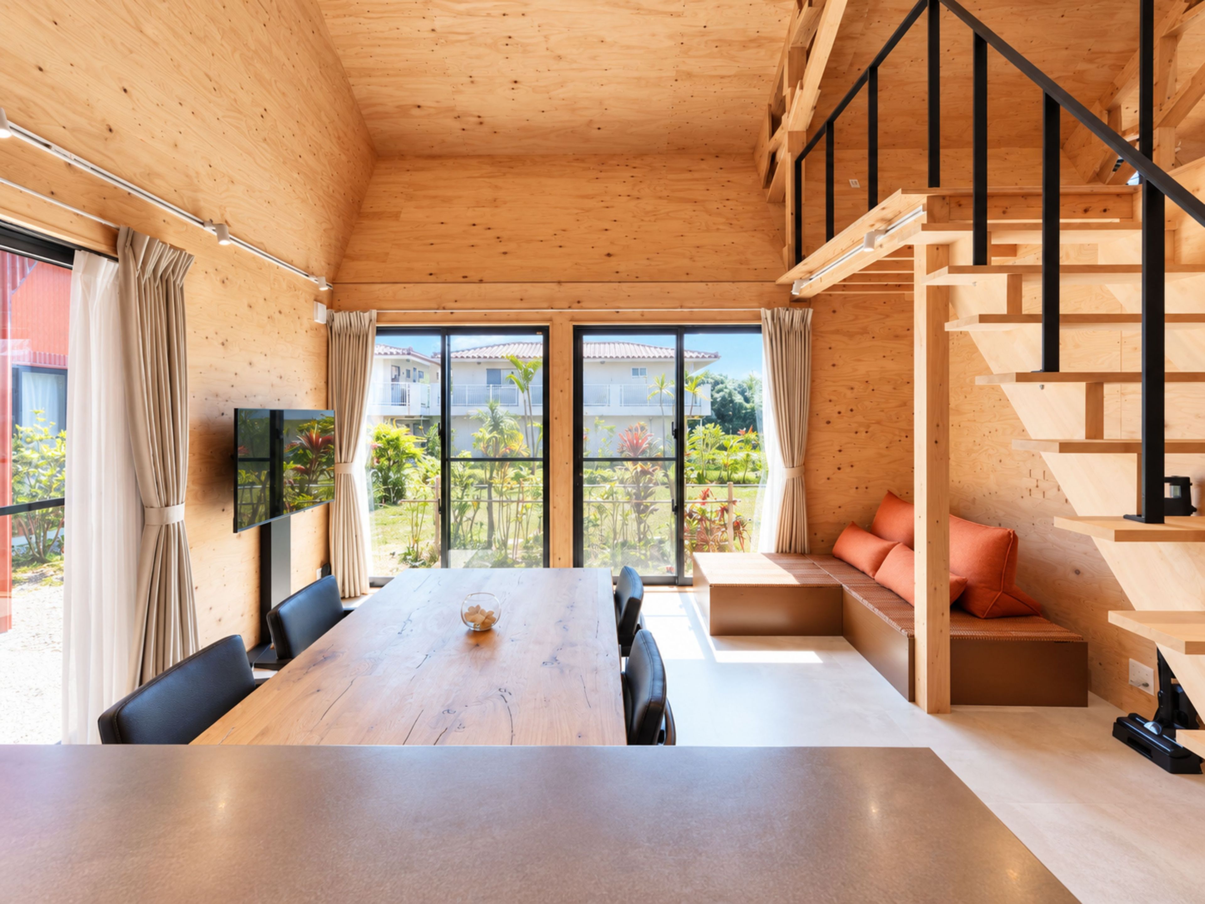 A modern interior with a wooden floor, a dining table, a sofa, and a staircase.