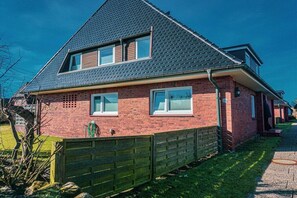 A two-story brick house with a sloped roof, a wooden fence, and a clear sky. - Holiday apartment with 2 bedrooms (Wenningstedt-Braderup)