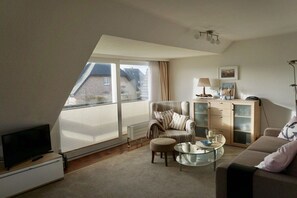 A modern living room with a television, sofa, armchair, glass coffee table, and a cabinet. - Holiday apartment with 2 bedrooms (Wenningstedt-Braderup)