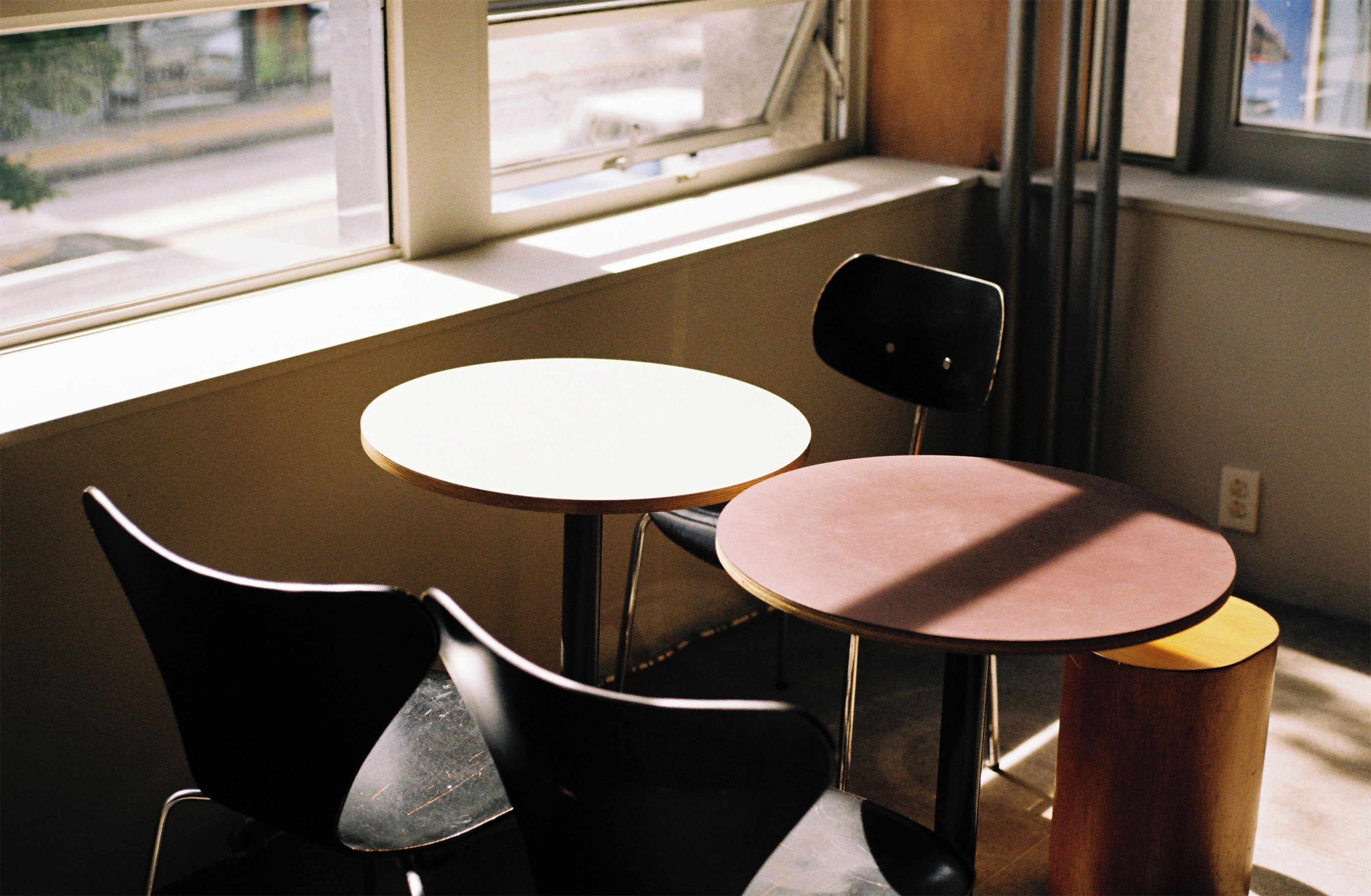 A small, enclosed seating area with two tables and chairs, a window, and a view of the street outside.