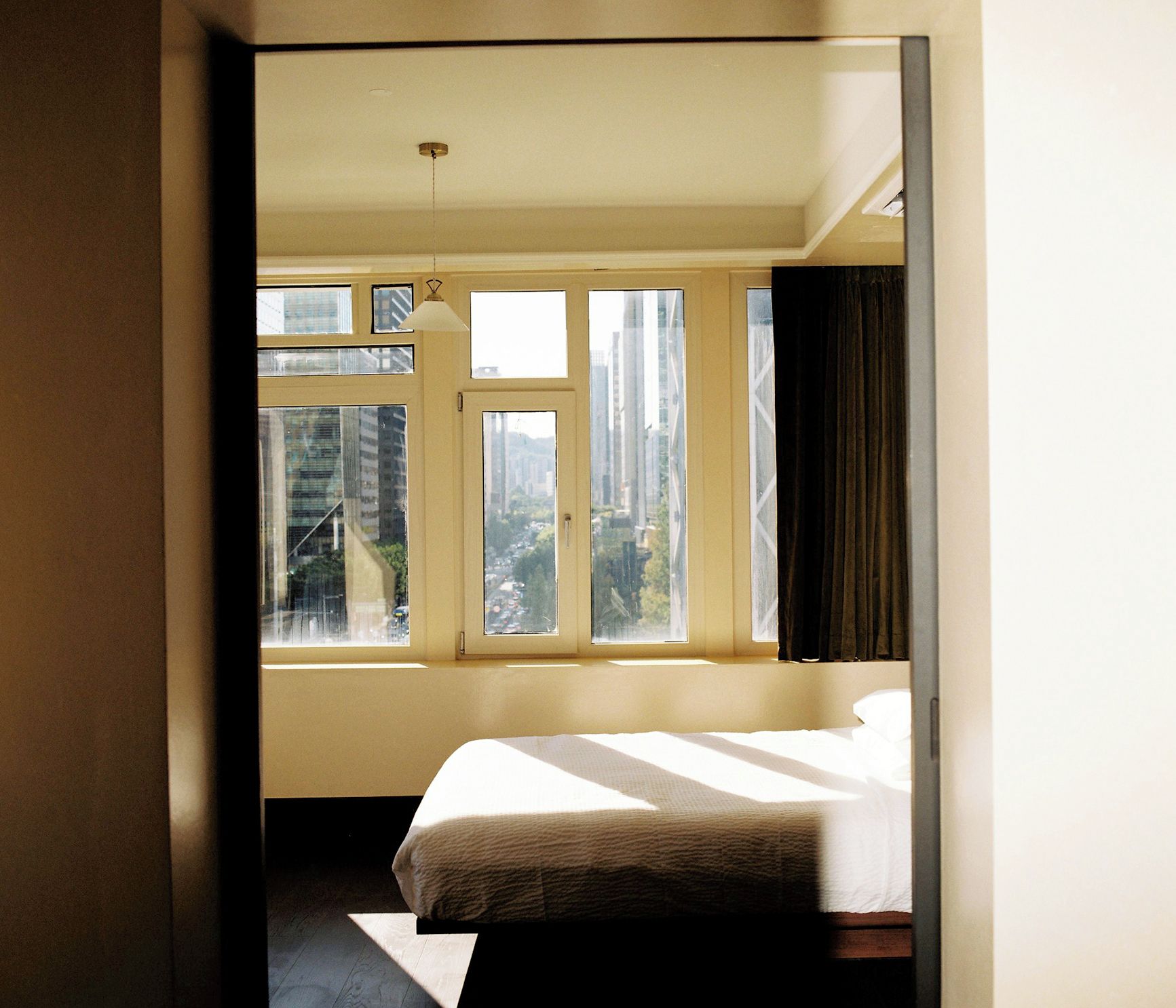 Una habitación de hotel con cama, ventana con cortinas y vista a edificios.