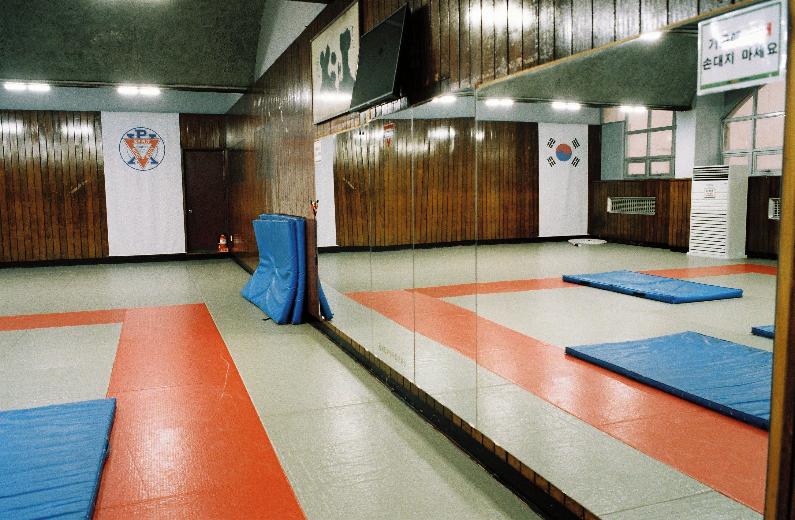 A martial arts training room with padded mats, wooden walls, and a flag.