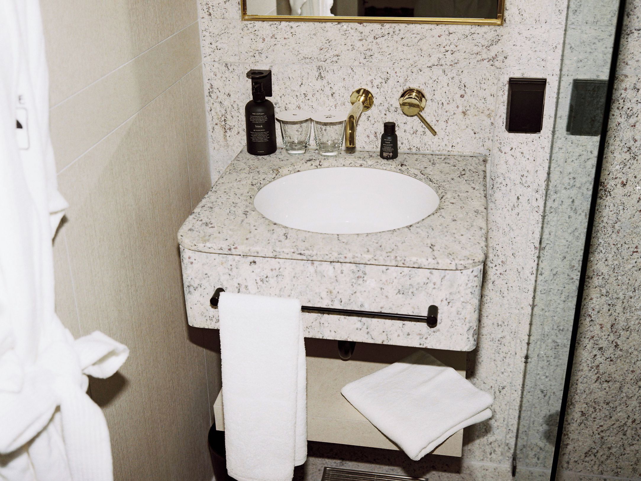 A bathroom with a granite countertop sink, a towel rack, and a mirror with a gold frame.