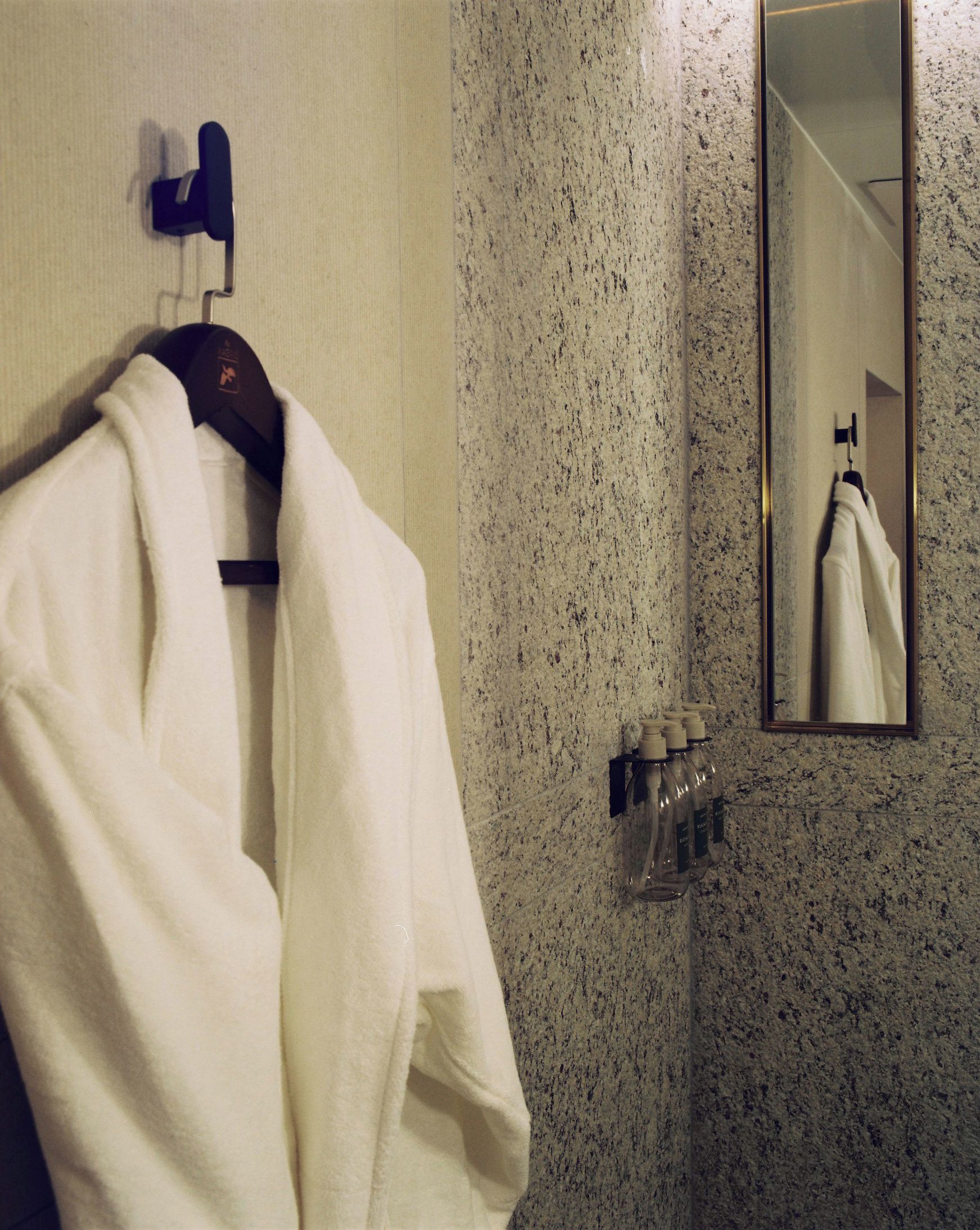 A bathroom with a towel hanging on a rack, a mirror, and a soap dispenser on the wall.