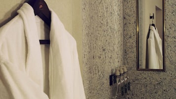 A bathroom with a towel hanging on a rack, a mirror, and a soap dispenser on the wall.