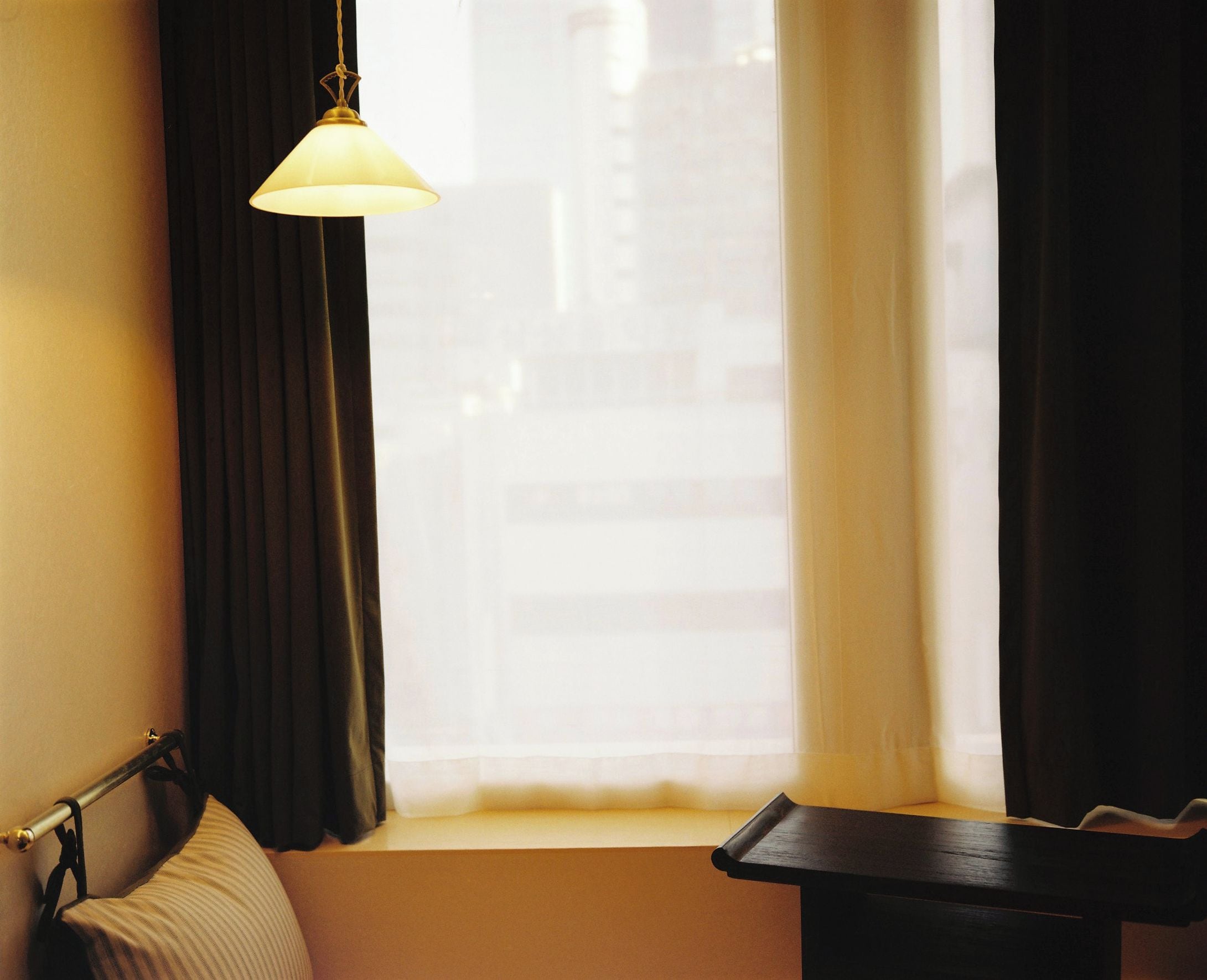 Una habitación de hotel con ventana, una cama, una mesita de noche y una lámpara colgante.