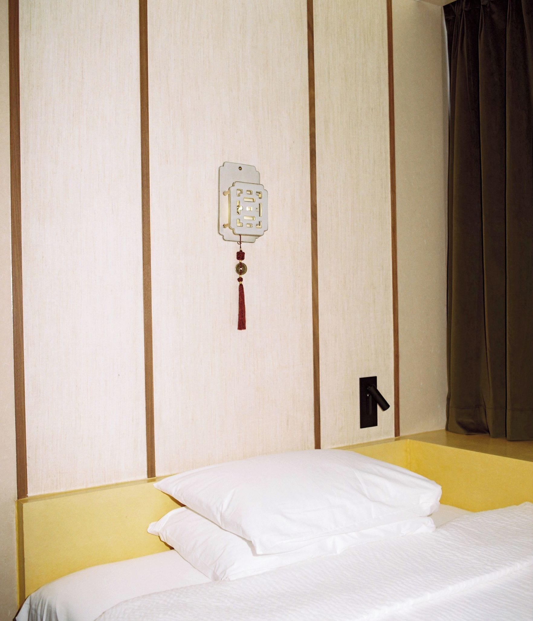A hotel room with a bed, a wall-mounted light switch, and a curtain.
