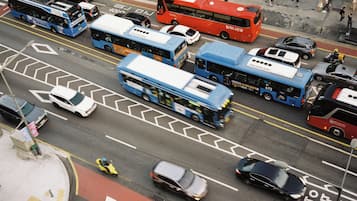 Uma rua movimentada no centro da cidade, com vários ônibus e carros, faixas de pedestres e sinalização viária clara.