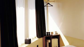 Une chambre d’hôtel avec un lit, une fenêtre avec des rideaux, une table de chevet avec une boîte de mouchoirs et un porte-manteau.