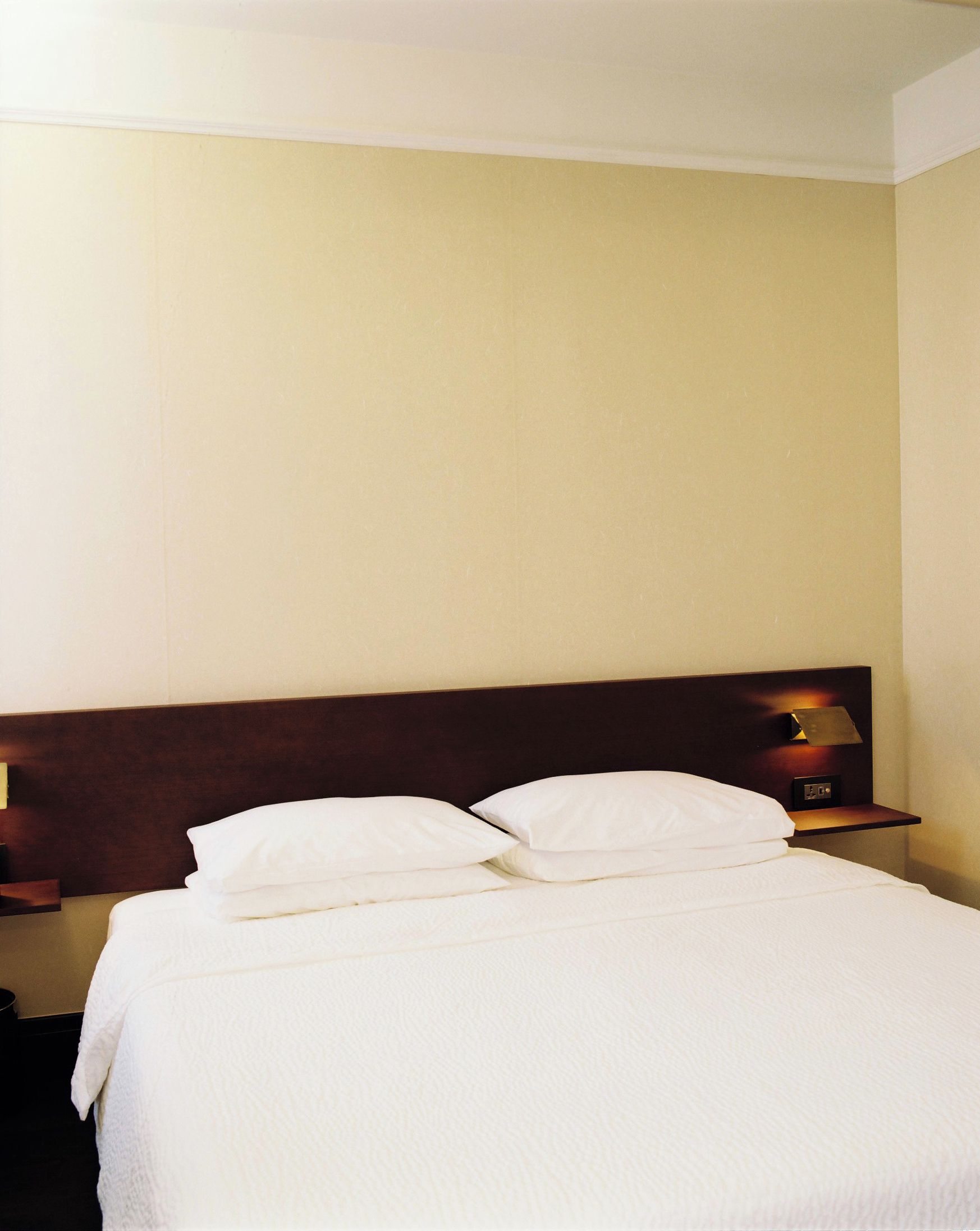 Ein Hotelzimmer mit einem Bett, Kissen, einem Nachttisch und einer Wandlampe.