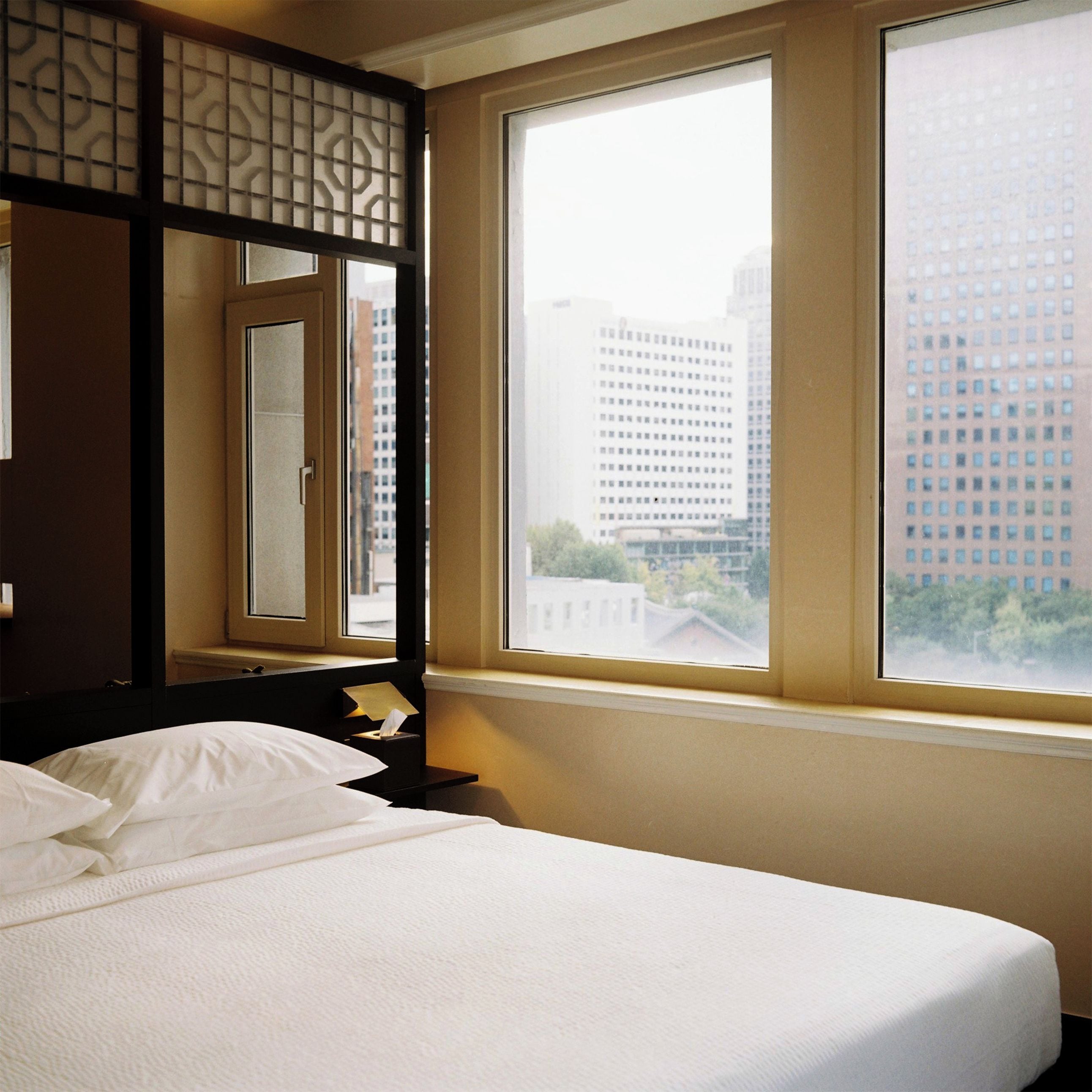 Ein Hotelzimmer mit Bett, Nachttisch, Spiegel und Fenster mit Blick auf die Stadt.