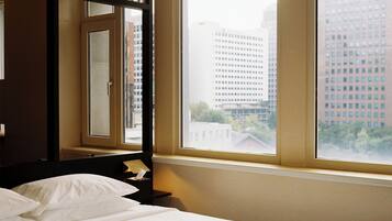 Ein Hotelzimmer mit Bett, Nachttisch, Spiegel und Fenster mit Blick auf die Stadt.
