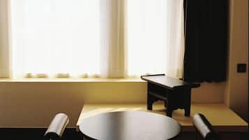 Una habitación con una mesa redonda y dos sillas, un pequeño banco, una lámpara colgante y una ventana con cortinas.