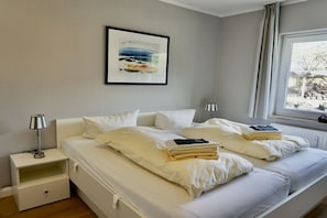 Ein Schlafzimmer mit einem Bett, Nachttischen, einer Lampe, einem gerahmten Bild und einem Fenster.