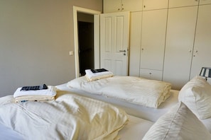 A bedroom with two beds, a wardrobe, and a door leading to another room. - House Rungholt Holiday Apartment 8 (Wenningstedt-Braderup)
