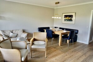 A dining area with a wooden table, blue chairs, and a woven chair. - House Rungholt Holiday Apartment 8 (Wenningstedt-Braderup)