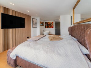A modern bedroom with a large bed, a flat-screen TV mounted on the wall, and a wooden panel design on the wall. - Modern Elegance at Residence 41 - Heart of Bastogne (Bastogne)